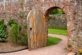 1778650-old-open-arched-wooden-door-set-into-an-old-red-brick-wall-and-leading-to-a-grassed-area-beyond
